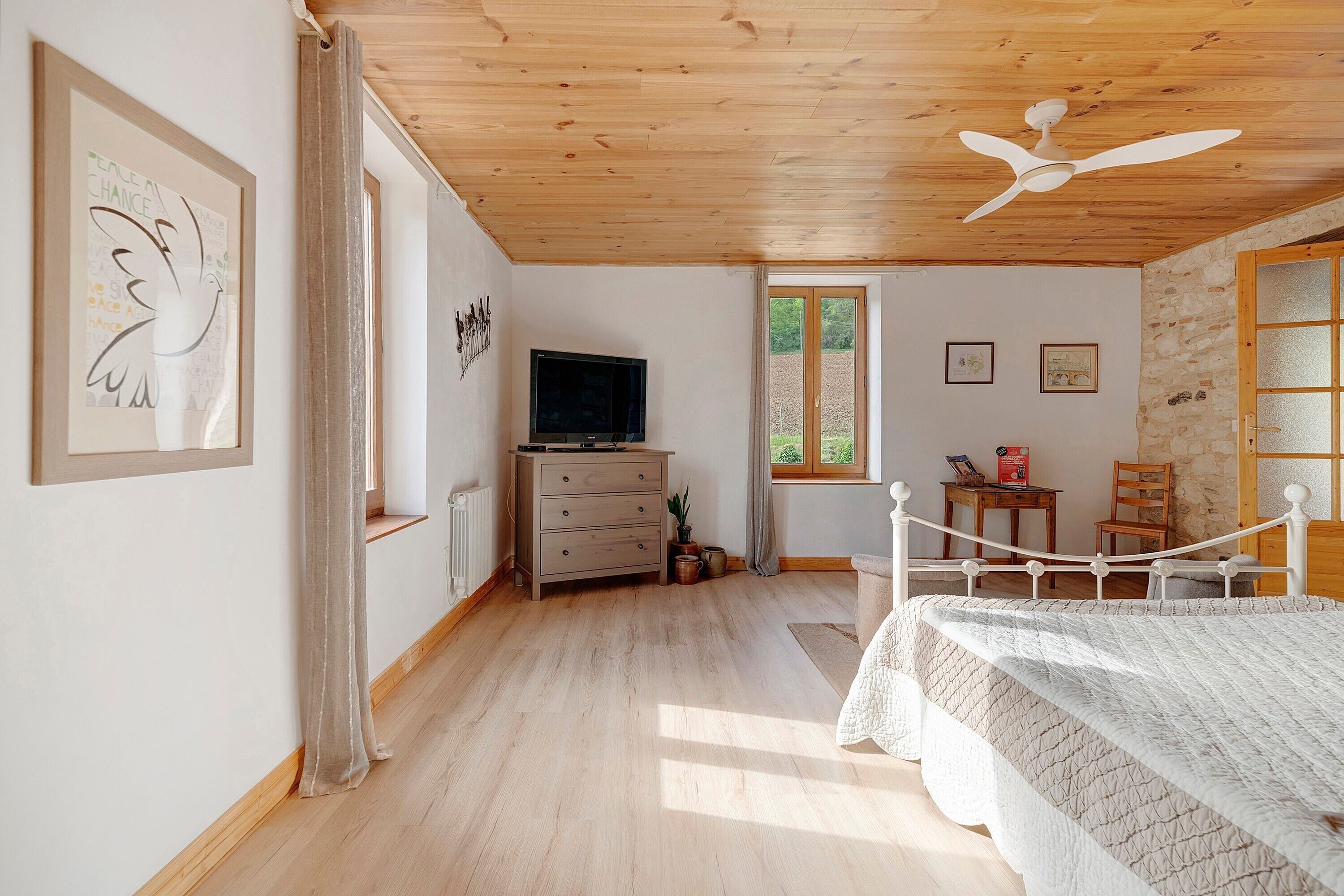 A bedroom with a bed, a dresser, a television, and a window.