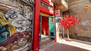 A red building with a green door, a mural on the wall, and a sign for 'MERGE Hostel'. - “Merge Hostel Chinatown — Hidden Chinese Stay in the heart of Yaowarat”​ (Krung Thep Maha Nakhon)