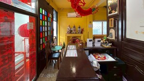 A restaurant interior with a long counter, chairs, a table with a menu, and a decorative red hanging ornament. - “Merge Hostel Chinatown — Hidden Chinese Stay in the heart of Yaowarat”​ (Krung Thep Maha Nakhon)