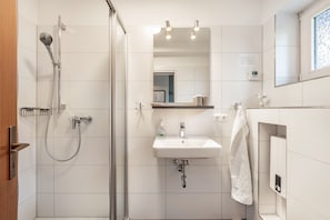 Ein Badezimmer mit Dusche, Waschbecken, Spiegel und Handtuchhalter.