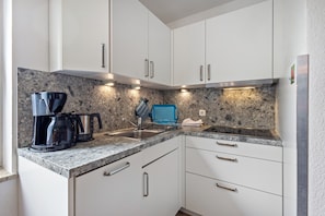 A kitchen with white cabinets, a granite countertop, a coffee maker, and a kettle.