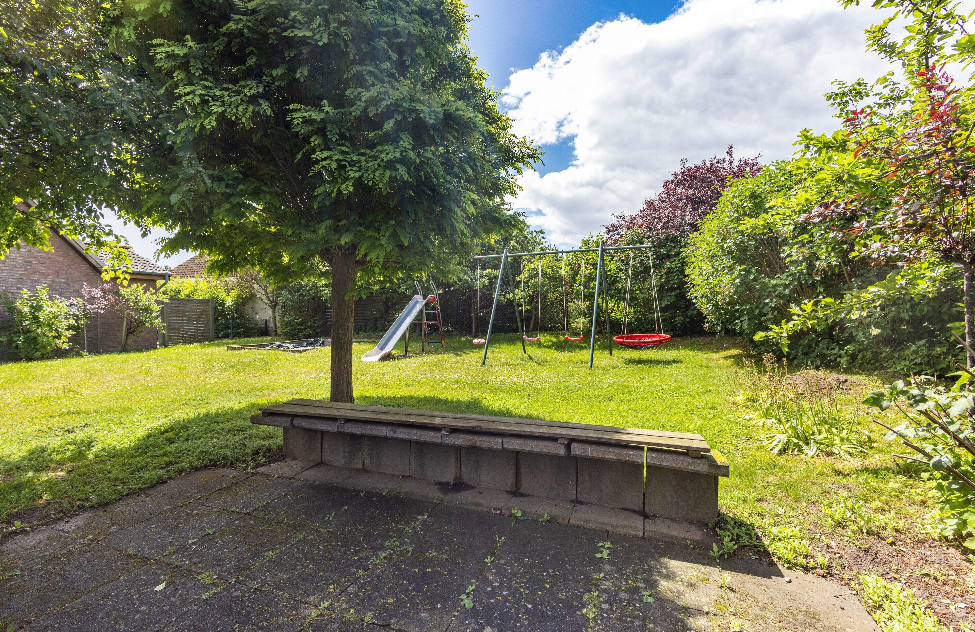 A backyard with a swing set, a slide, a bench, and a tree.