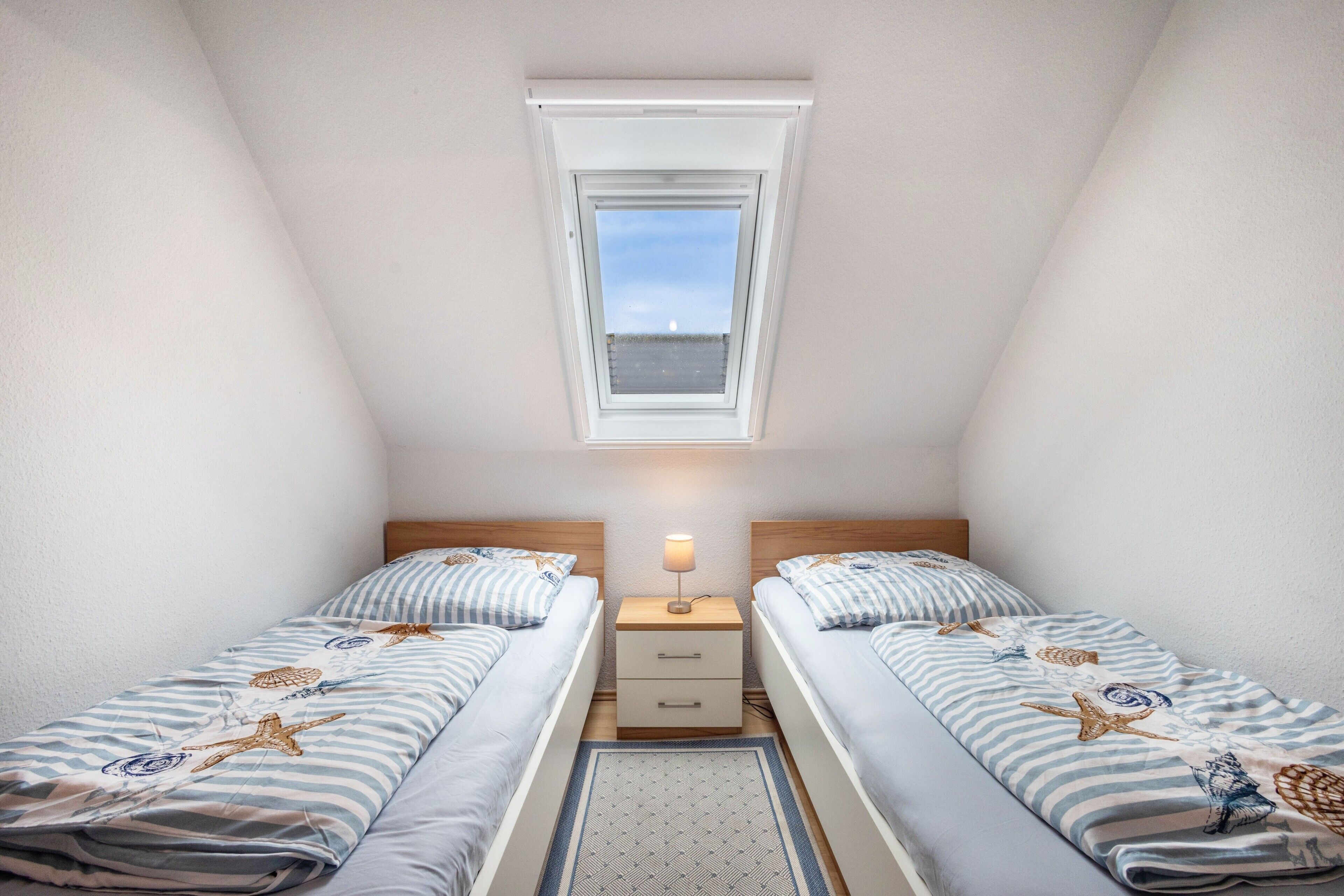 Ein Doppelzimmer mit zwei Betten, einem Nachttisch, einer Lampe, einem Fenster und Blick auf den Himmel.