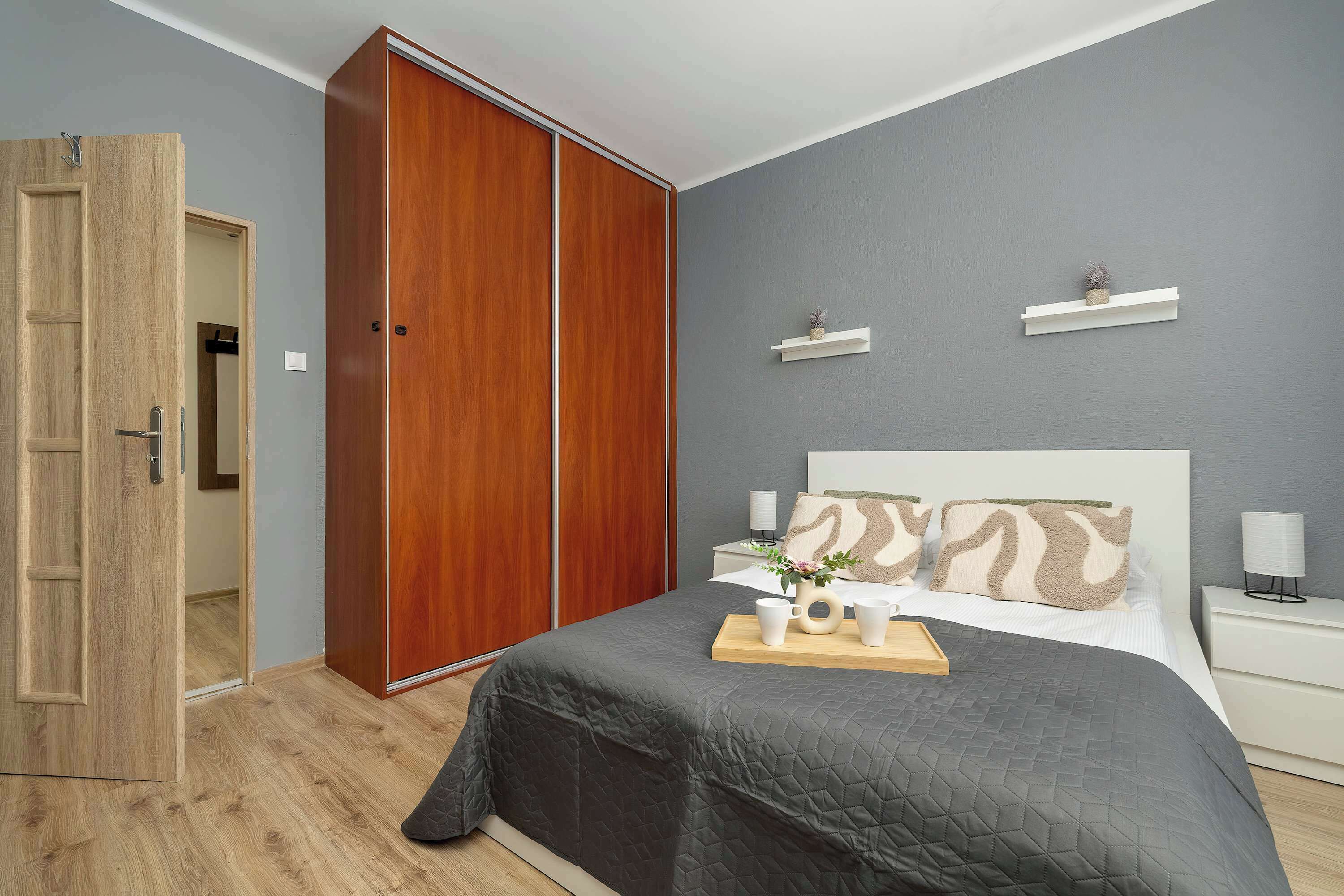 Un dormitorio con cama, mesitas de noche, un armario y una pequeña estantería con una planta.