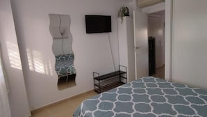 A bedroom with a bed, a TV mounted on the wall, a mirror, and a door leading to another room. - Relax & Play Panoramic Golf Vinaroz (San Jorge)