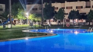 A swimming pool with a circular design, surrounded by palm trees and a building with multiple windows. - Relax & Play Panoramic Golf Vinaroz (San Jorge)