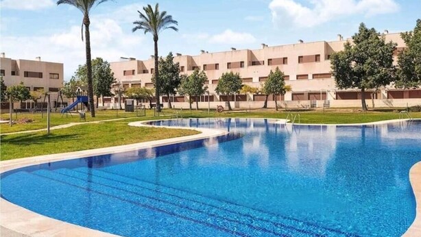 A swimming pool with a curved edge, surrounded by a grassy area and palm trees. - Relax & Play Panoramic Golf Vinaroz (San Jorge)