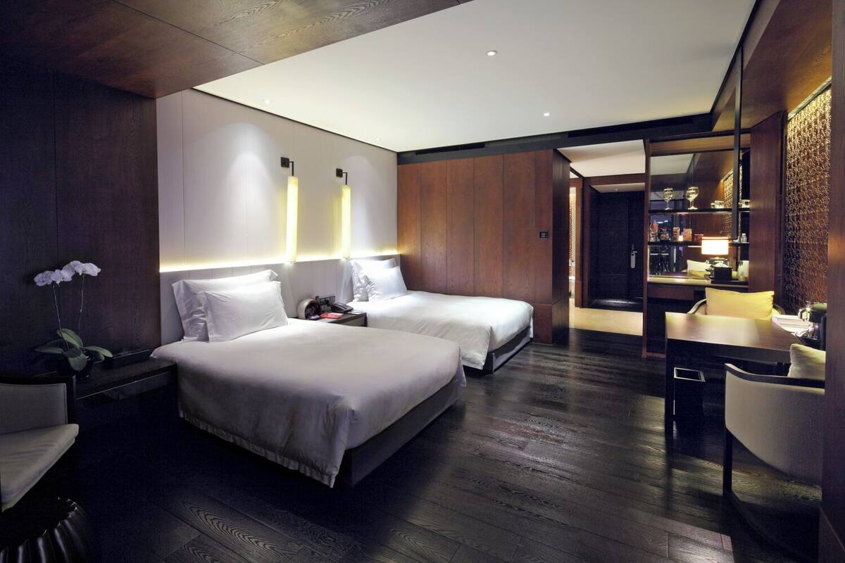 A modern hotel room with two beds, a desk, and a dining area.