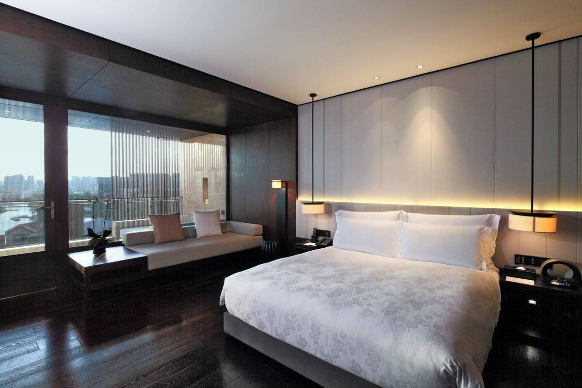 A modern hotel room with a large bed, a seating area by the window, and a city view.