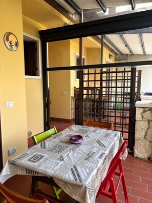 Uma área de refeições com uma mesa coberta por um tecido estampado, cadeiras e um objeto decorativo na parede.