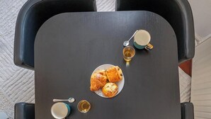 Uma mesa com doces e xícaras, rodeada por cadeiras pretas.