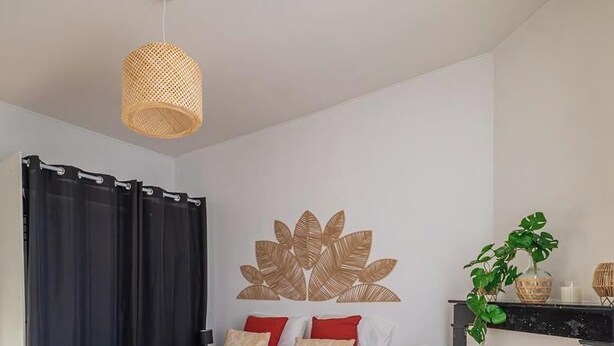 Quarto com cama, cortina preta, planta suspensa na parede e luminária trançada.