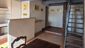 A kitchen with a stove, a wooden counter, and a chair. There are framed pictures on the wall and a staircase to the right. - Le Buis Authentic village house 4 people (Aiguines)
