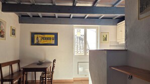 A dining area with a wooden table and chairs, a bench, a radiator, and a window with a view of buildings. - Le Buis Authentic village house 4 people (Aiguines)