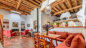 Un interior rústico con vigas de madera a la vista, una mesa de comedor de madera, sillas rojas y un colgante de luz.