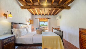 Un dormitorio con techo de madera, una cama con ropa de cama blanca, una mesita de noche, una lámpara y vistas al exterior.