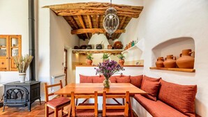 Una habitación acogedora con una mesa de madera, asientos con cojines rojos, una lámpara colgante y cerámica en estantes.