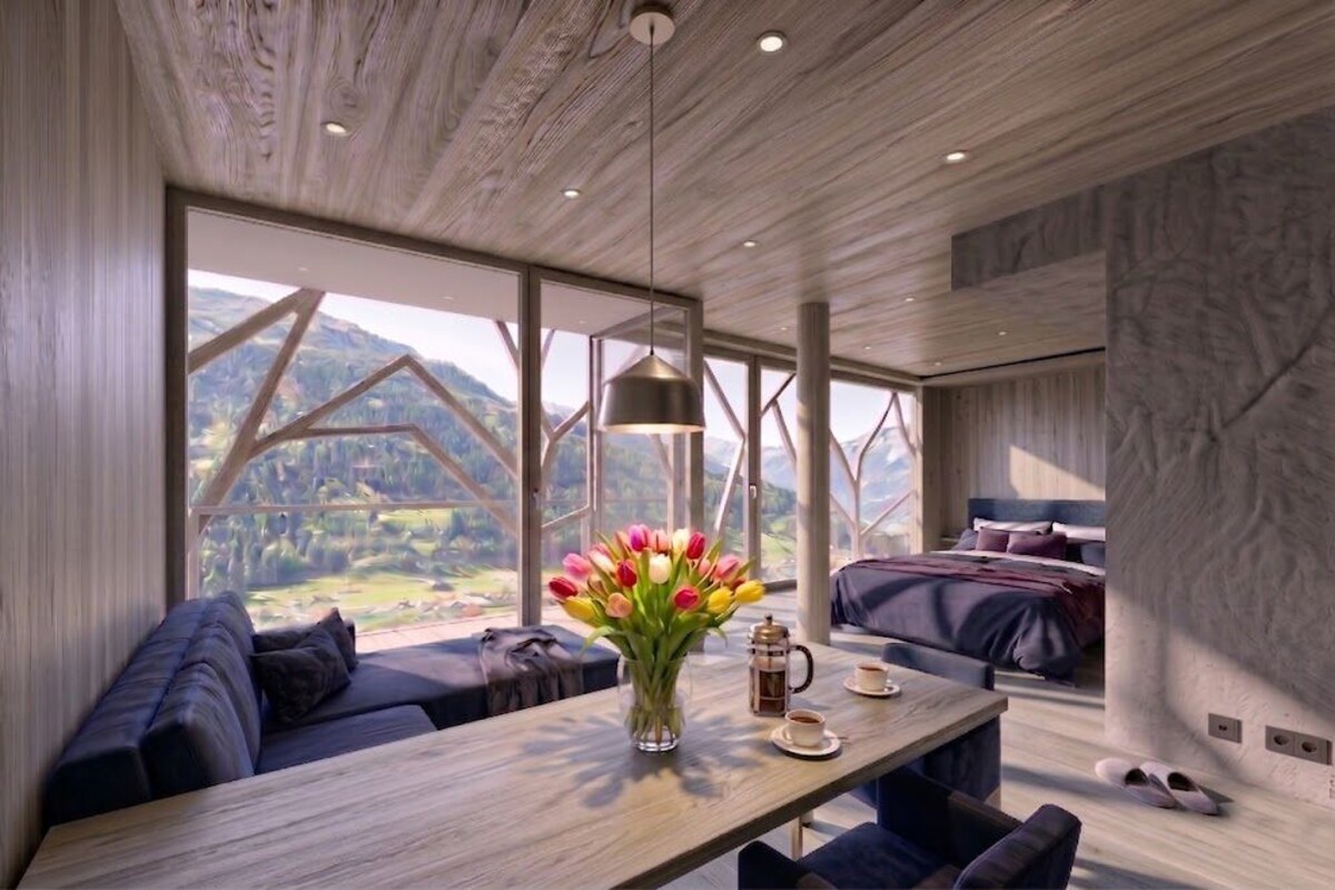 Quarto moderno com teto de madeira, janelas amplas, uma cama, um sofá, uma mesa com um vaso de flores e uma cafeteira.