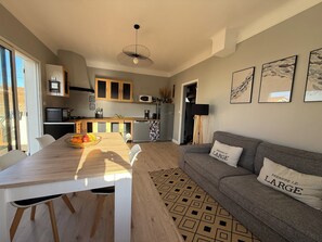 A modern kitchen with a dining table, a grey sofa with a large pillow, and a patterned rug. - House just a stone's throw from the sea. 350 meters from the beach. (La Plaine-sur-Mer)