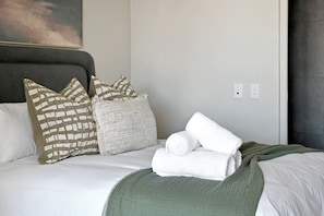 A neatly made bed with pillows, a rolled white towel, and a green throw blanket. - Soft Luxury in CBD with Table Mountain views and AC (Cape Town)