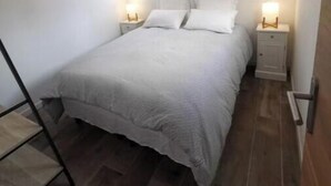 Un dormitorio con cama, mesitas de noche, lámpara colgante, ventana y puerta.
