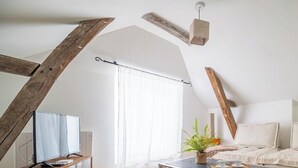 Una habitación con techo inclinado, una cama con almohadas, una mesa con planta y un televisor sobre un mueble.