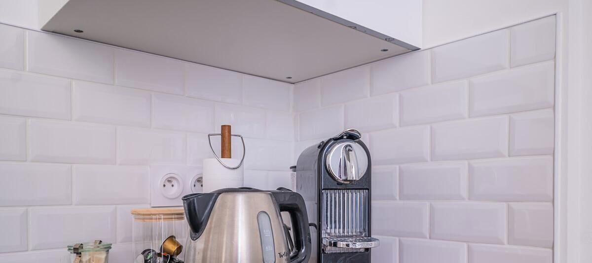 Eine Küche mit weiß gefliesten Wänden, einer Kaffeemaschine und einem Wasserkocher.