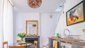 Una cocina moderna con armarios blancos, una mesa de comedor con sillas, una chimenea y una lámpara colgante.
