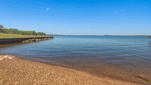 A calm lake with a pebbled shore and a wooden dock extending into the water. - Lakefront Retreat Paradise (Pittsburg)