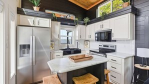 A kitchen with white cabinets, a marble countertop, a stainless steel refrigerator, a microwave, and wooden stools. - Lakefront Retreat Paradise (Pittsburg)