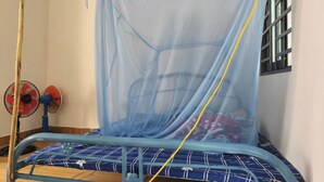 Un lit doté d’une moustiquaire, d’un cadre en métal bleu et d’un ventilateur rouge et blanc.