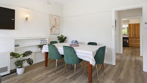 Et spiseområde med et bord dækket til fire personer, grønne polstrede stole, et hvidt borddække og et billede på væggen.