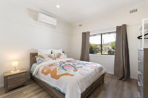 A bedroom with a bed, a nightstand, a window with curtains, and an air conditioning unit. - Sherbrooke, Rosebud. (Rosebud)