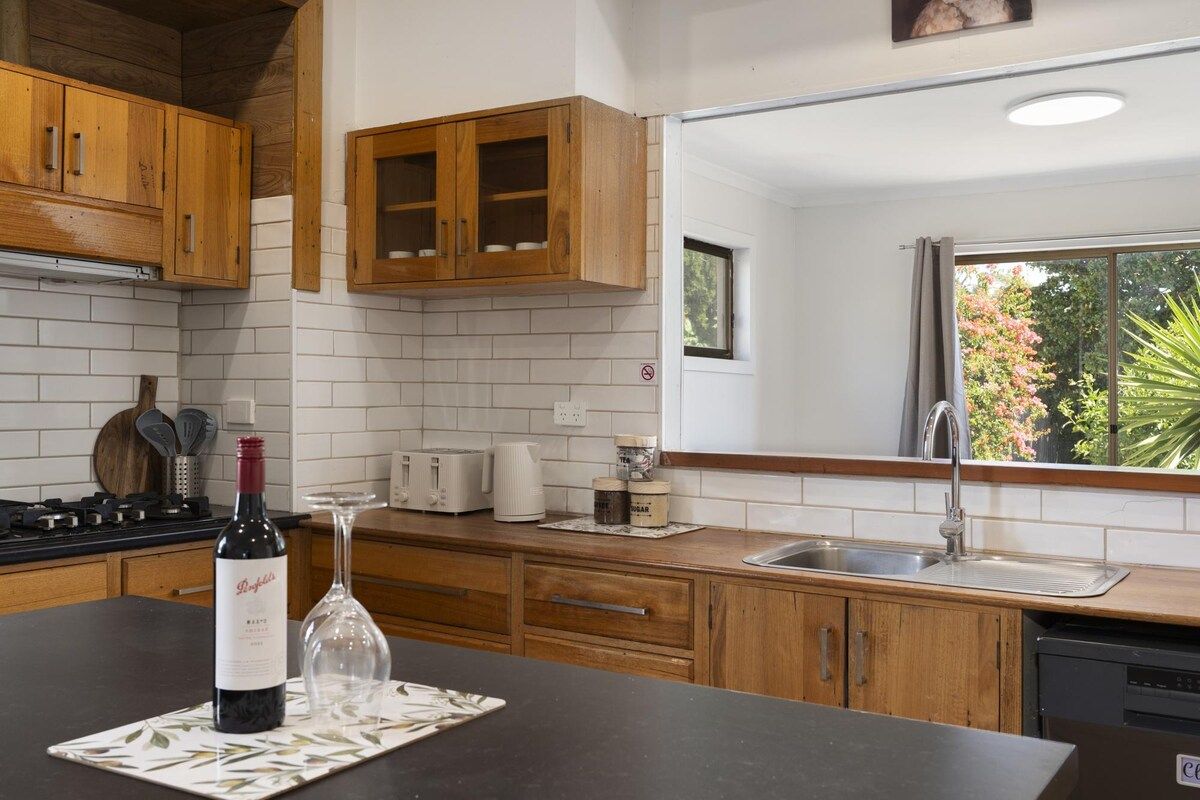 A kitchen with wooden cabinets, a wine bottle, and a glass on a mat.