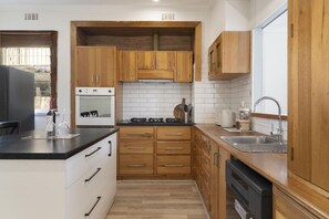 A kitchen with wooden cabinets, a black countertop, a built-in oven, and a dishwasher. - Sherbrooke, Rosebud. (Rosebud)