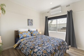 A bedroom with a bed, a window with curtains, an air conditioning unit, and a wall-mounted artwork. - Sherbrooke, Rosebud. (Rosebud)