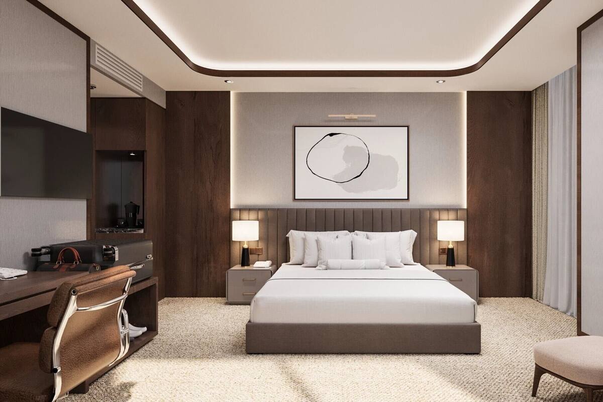 A modern hotel room with a large bed, a desk, a chair, and a wall-mounted artwork.