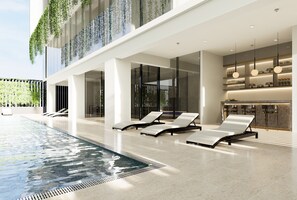 Un espace piscine intérieur moderne, doté de chaises longues, d’un comptoir d’accueil et d’un espace clos par des parois de verre.