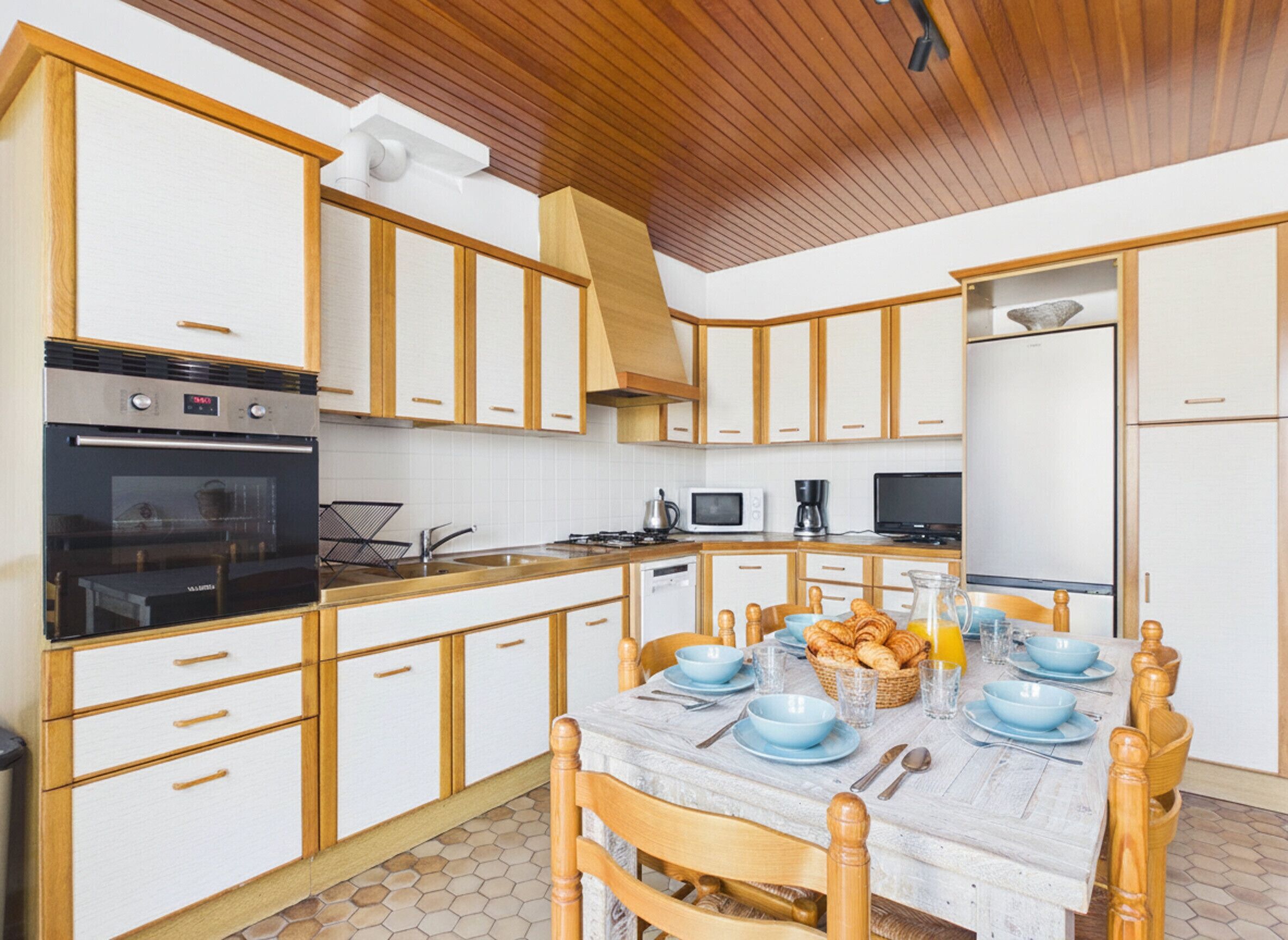 Una cocina con armarios de madera, una mesa de comedor preparada para cuatro personas y un microondas.