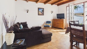 Ein Wohnzimmer mit einer Couch, einem Fernseher, einem Holzkasten und einem Sessel.