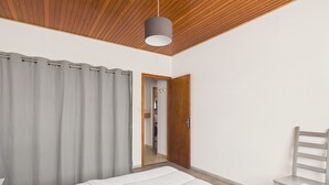 Ein Schlafzimmer mit einem Bett, einem Sessel, einer Holzbalkendecke und einer Tür zu einem anderen Raum.