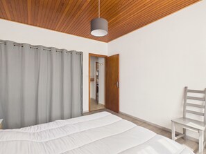 Un dormitorio con cama, una silla, techo de madera y una puerta que da a otra habitación.