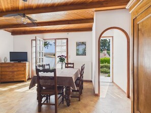 Un área de comedor con una mesa, sillas, un televisor sobre un mueble de madera y vista a través de una puerta abierta.