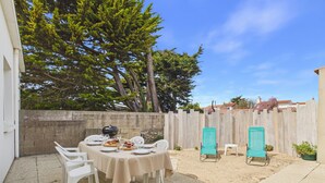 Eine Terrasse mit Esstisch, umgeben von Stühlen, einem Grill und einem Holzzaun.