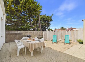 Un patio con mesa lista para una comida, rodeado de sillas, una parrilla y una valla de madera.