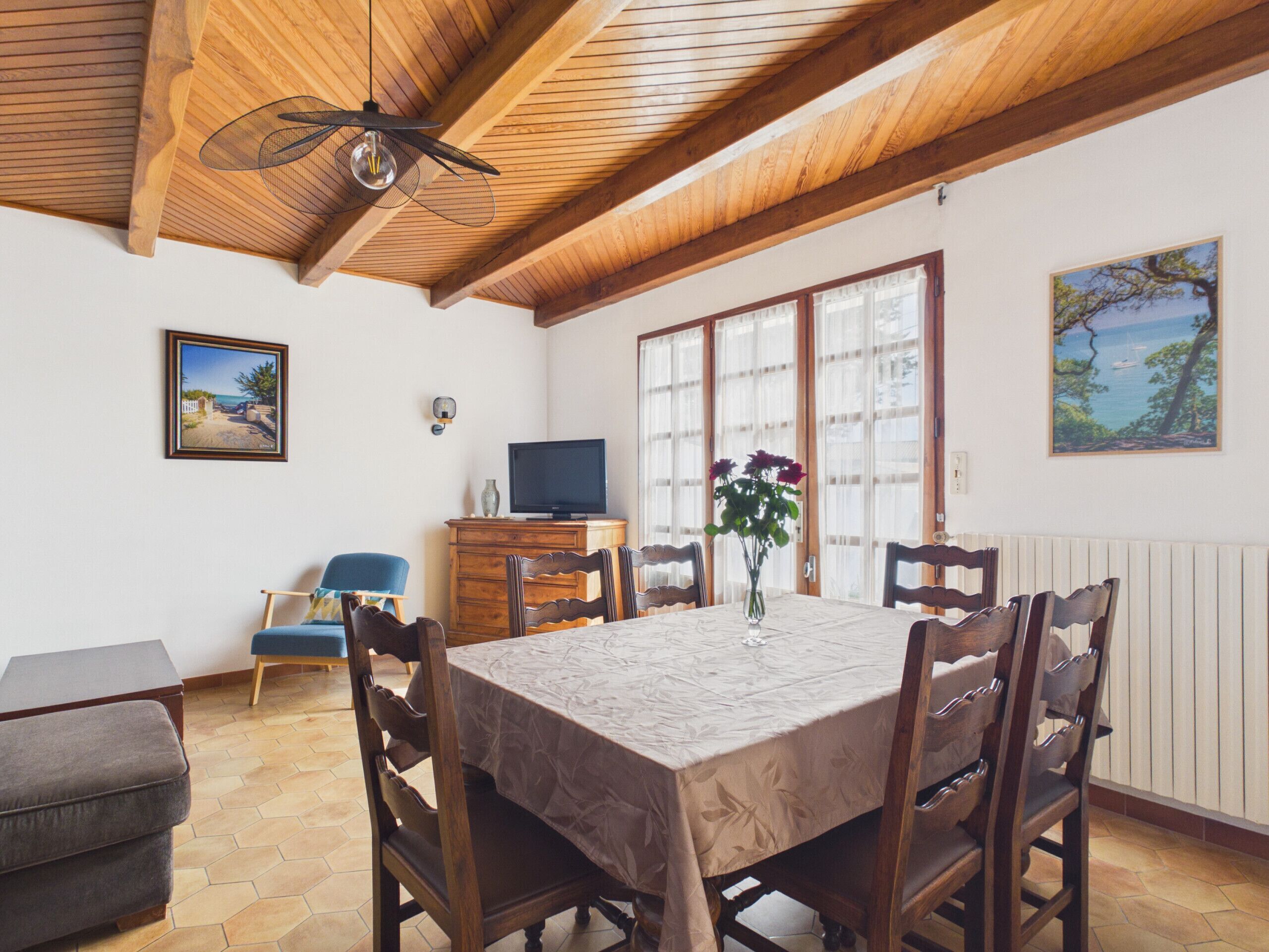A dining area with a table, chairs, a television, and a vase with flowers.