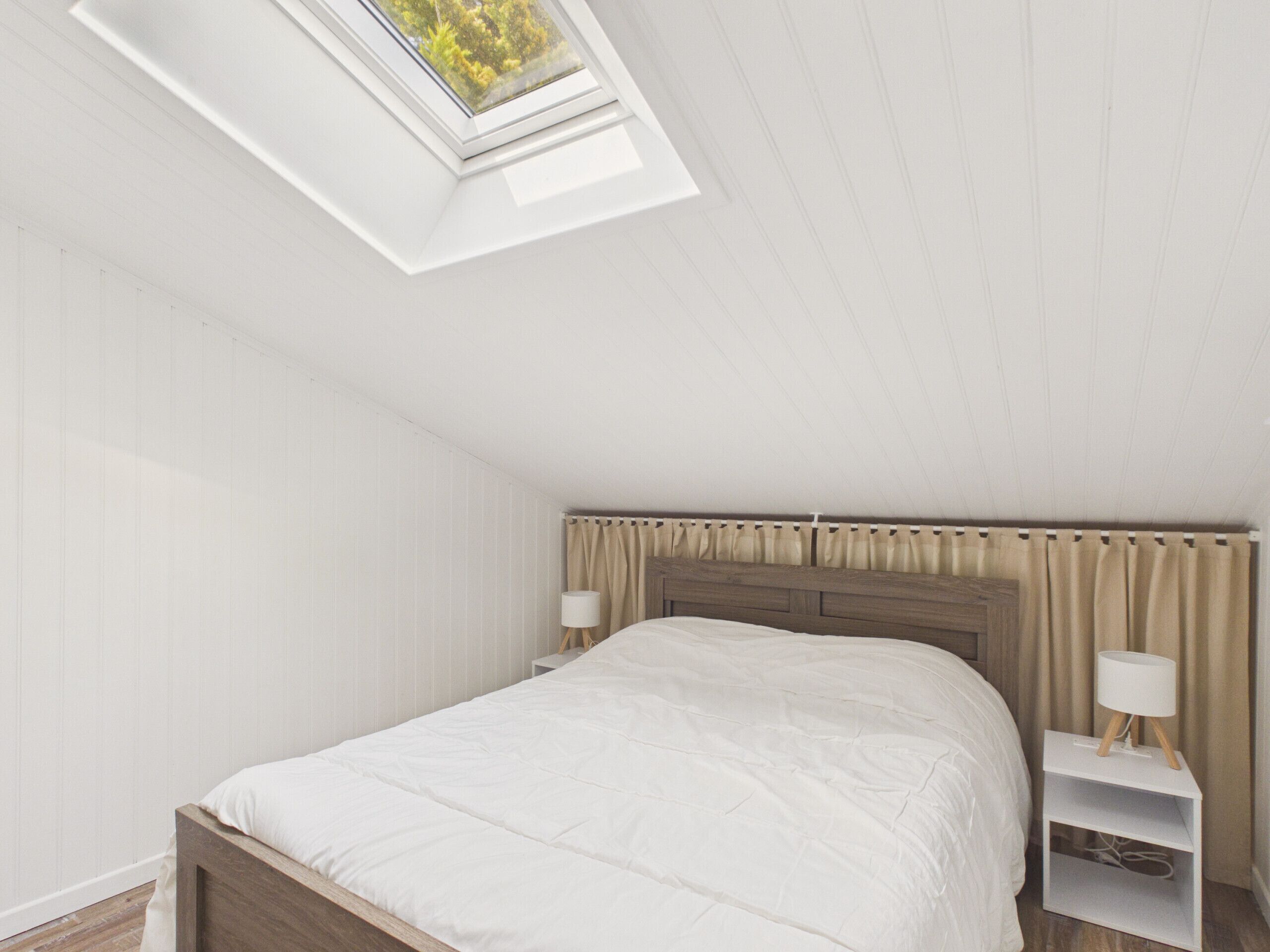 Une chambre à coucher avec un puits de lumière, un lit, une table de chevet avec une lampe et une tête de lit en bois.