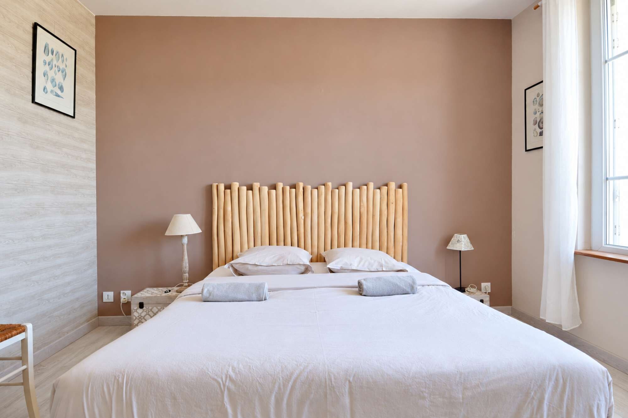 A hotel room with a large bed, two bedside lamps, a wooden headboard, and a window with curtains.