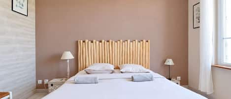 A hotel room with a large bed, two bedside lamps, a wooden headboard, and a window with curtains.