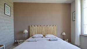 Een hotelkamer met een groot bed, twee bedlampen, een hoofdbord met verticale lamellen en een raam met gordijnen.